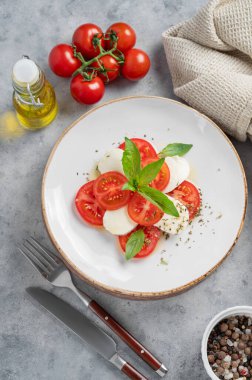 Dilimlenmiş domatesli Caprese salatası, mozzarella ve arka planda hafif bir tabakta zeytinyağı ve sebzeli fesleğen. Sağlıklı Akdeniz mutfağı konsepti. Üst görünüm.