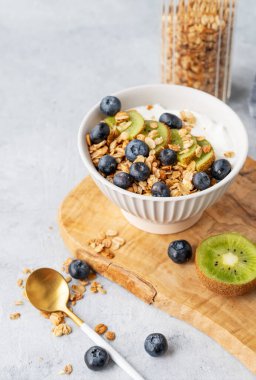Tahta bir tahtanın üzerinde taze böğürtlenli doğal yoğurt, kivi ve yaban mersini kasesi. Sağlıklı ve besleyici kahvaltı konsepti. Boşluğu kopyala.