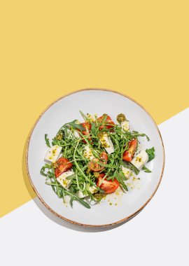 Çeri domatesli taze roka salatası, mozzarella, beyaz sarı arka planda pesto sosu. Taze ve sağlıklı Akdeniz mutfağı kavramı. Üst görünüm ve kopyalama alanı.
