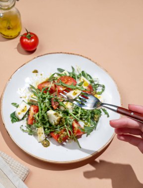El ele tutuşan taze roka salatası, kiraz domatesleri, mozzarella, bej arka planda pesto sosu. Taze ve sağlıklı Akdeniz mutfağı kavramı. Üst görünüm ve kopyalama alanı.