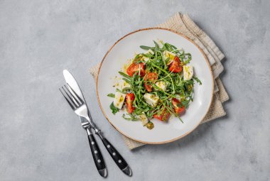 Kiraz domatesli Arugula salatası, mozzarella ve arka planda peçete ve çatal bıçaklı pesto sosu. Taze ve sağlıklı Akdeniz gıda konsepti. Üst görünüm, alanı kopyala.