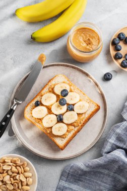 Fıstık ezmeli, muzlu ve yaban mersinli tost fındıklı ve sabah gölgeli bir tabakta. Amerikan kahvaltısı için tatlı diyet ve sağlıklı atıştırmalıklar kavramı. Üst görünüm.