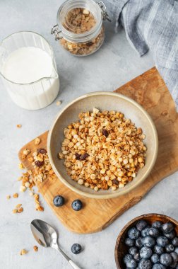 Süt yaban mersini ve kaşıkla arka planda, ahşap bir tahtanın üzerinde ev yapımı granola ya da müsli. Sağlıklı ve besleyici kahvaltı konsepti. Üst görünüm.
