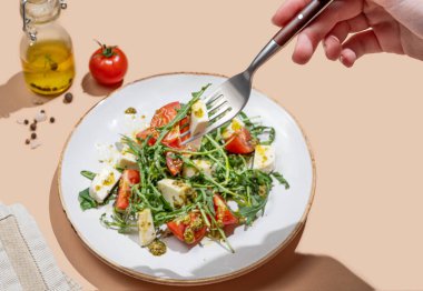 El ele tutuşan taze roka salatası, kiraz domatesleri, mozzarella, bej arka planda pesto sosu. Taze ve sağlıklı Akdeniz mutfağı kavramı. Üst görünüm ve kopyalama alanı.