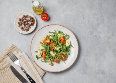 Kiraz domatesli Arugula salatası, mozzarella ve arka planda peçete ve çatal bıçaklı pesto sosu. Taze ve sağlıklı Akdeniz gıda konsepti. Üst görünüm, alanı kopyala.