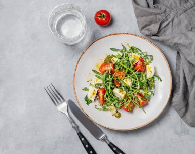 Kiraz domatesli Arugula salatası, mozzarella ve bir bardak su ve çatal bıçakla arka planda pesto sosu. Taze ve sağlıklı Akdeniz gıda konsepti. Üst görünüm, alanı kopyala.