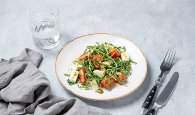 Kiraz domatesli Arugula salatası, mozzarella ve bir bardak su ve çatal bıçakla arka planda pesto sosu. Taze ve sağlıklı Akdeniz gıda konsepti. Boşluğu kopyala.