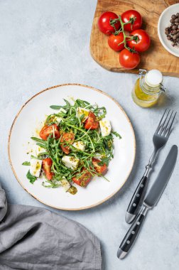 Kiraz domatesli Arugula salatası, mozzarella ve arka planda peçete ve çatal bıçaklı pesto sosu. Taze ve sağlıklı Akdeniz gıda konsepti. Üst görünüm, alanı kopyala.