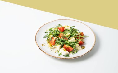 Çeri domatesli taze roka salatası, mozzarella, beyaz sarı arka planda gölgeli pesto sosu. Taze ve sağlıklı Akdeniz mutfağı kavramı. Boşluğu kopyala.