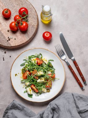 Kiraz domatesli sağlıklı roka salatası, mozzarella ve peçete ve çatal bıçakla hafif bir arka planda pesto sosu. Taze ve sağlıklı Akdeniz gıda konsepti. Üst görünüm, alanı kopyala.