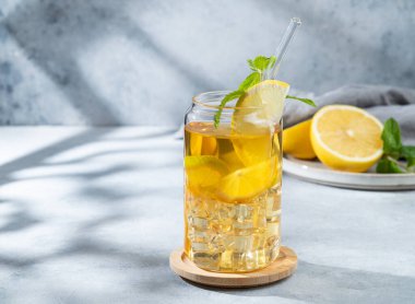 Limonlu buzlu içecek ve hafif arka planda bir bardakta nane şekeri. Gölgeler ve narenciye meyveleriyle. Bir yaz günü soğuk çay ya da limonata konsepti. Ön görünüm, boşluğu kopyala.