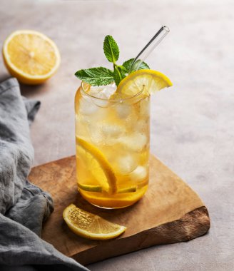 Limonlu buzlu çay ve narenciyeli hafif bir arka planda, tahta bir tahtanın üzerinde bir bardak nane şekeri. Yaz günü ferahlatıcı içecek ya da limonata konsepti. Boşluğu kopyala.
