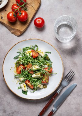Kiraz domatesli sağlıklı roka salatası, mozzarella ve bir bardak suyla arka planda pesto sosu. Taze ve sağlıklı Akdeniz gıda konsepti. Üst görünüm, alanı kopyala.
