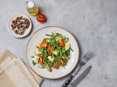 Kiraz domatesli Arugula salatası, mozzarella ve arka planda peçete ve çatal bıçaklı pesto sosu. Taze ve sağlıklı Akdeniz gıda konsepti. Üst görünüm, alanı kopyala.