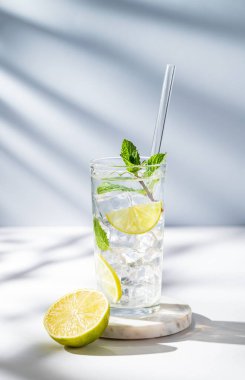 Limonlu, naneli, buzlu ve gölgeli beyaz mavi bir fonda mojito kokteyli. Turunçgil meyveleriyle ferahlatıcı limonata içeceği konsepti. Ön görünüm, boşluğu kopyala