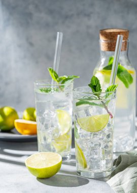 İki bardak mojito kokteyli. Taze limonlu, naneli ve buzlu. Arka planda hafif bir şişe ve gölge var. Turunçgil meyveli yaz ferahlatıcı içecek konsepti. Ön görünüm.