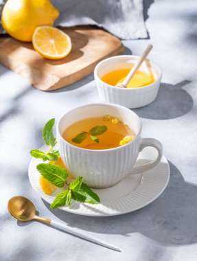 Limon, bal ve nane arkaplanda narenciye ve sabah gölgeleriyle birlikte bir fincan bitki çayı. Kahvaltıda sağlıklı detoks içeceği kavramı. 