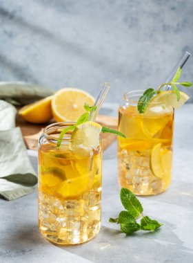 İki bardak buzlu içecek, limonlu ve nane arkaplanda gölgeli ve narenciye meyveli. Bir yaz günü soğuk çay ya da limonata konsepti. Ön görünüm, boşluğu kopyala.