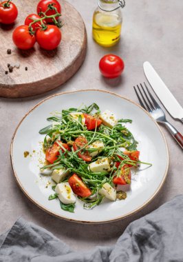 Kiraz domatesli sağlıklı roka salatası, mozzarella ve hafif arka planda sebze ve çatal bıçaklı pesto sosu. Taze ve sağlıklı Akdeniz gıda konsepti. Üst görünüm.