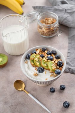 Mısır gevreği, kivi ve yaban mersinli yoğurt. Arka planda taze böğürtlen ve meyve var. Sağlıklı ve besleyici kahvaltı konsepti. Üst görünüm.