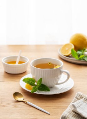 Limonlu, ballı ve nane şekerli bir fincan bitki çayı. Sabah ışıklarıyla pencereye yaslanmış narenciye meyveleriyle birlikte. Kahvaltıda sağlıklı detoks içeceği kavramı. Boşluğu kopyala.