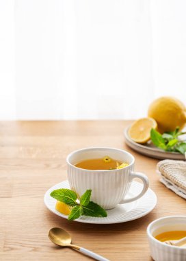 Limonlu, ballı ve naneli bir fincan bitki çayı. Sabah ışıklarıyla pencereye yaslanmış ahşap masa üstü. Kahvaltıda sağlıklı detoks içeceği kavramı. Boşluğu kopyala.