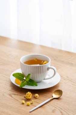 Limonlu, ballı ve naneli bir fincan bitki çayı. Sabah ışıklarıyla pencereye yaslanmış ahşap masa üstü. Kahvaltıda sağlıklı detoks içeceği kavramı. Boşluğu kopyala.
