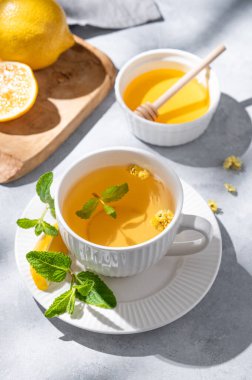 Limon, bal ve nane arkaplanda narenciye ve sabah gölgeleriyle birlikte bir fincan bitki çayı. Kahvaltıda sağlıklı detoks içeceği kavramı. 