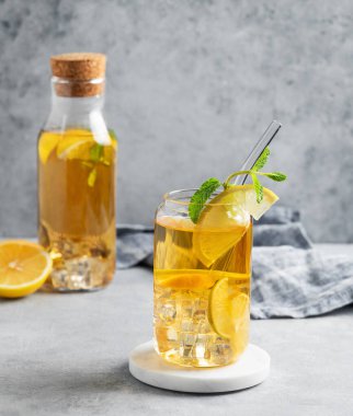 Limonlu buzlu içecek ve bardakta nane ve arka planda gölgeler ve narenciye meyveleriyle hafif bir şişe. Bir yaz günü soğuk çay ya da limonata konsepti. Ön görünüm, boşluğu kopyala.