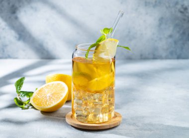 Limonlu buzlu içecek ve hafif arka planda bir bardakta nane şekeri. Gölgeler ve narenciye meyveleriyle. Bir yaz günü soğuk çay ya da limonata konsepti. Ön görünüm, boşluğu kopyala.
