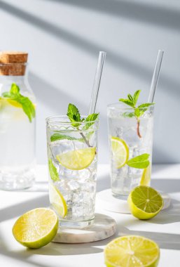 İki bardak mojito kokteyli, limon, nane, buz ve gölgeli hafif bir arka planda tüp. Turunçgil meyveleriyle ferahlatıcı limonata içeceği konsepti. Ön görünüm, boşluğu kopyala