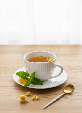 Limonlu, ballı ve naneli bir fincan bitki çayı. Sabah ışıklarıyla pencereye yaslanmış ahşap masa üstü. Kahvaltıda sağlıklı detoks içeceği kavramı. Boşluğu kopyala.