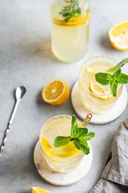 Limonlu, naneli ve buzlu iki bardak taze limonata. Arka planda hafif bir şişe, taze bitki ve meyve var. Yaz modasına uygun mojito mocktail konsepti. Üst görünüm, alanı kopyala