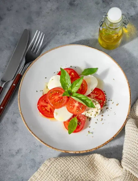 Dilimlenmiş domatesli Caprese salatası, mozzarella ve doğal ışıkta peçeteli beyaz arka planda bir tabakta fesleğen. Sağlıklı Akdeniz mutfağı konsepti. Üst görünüm ve kopyalama alanı.
