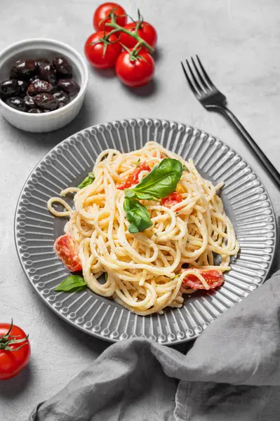 Çeri domatesli lezzetli kremalı spagetti, parmesan peyniri ve zeytinli gri dokulu bir tabakta fesleğen. İtalyan ya da Akdeniz mutfağı konsepti. Üst görünüm.
