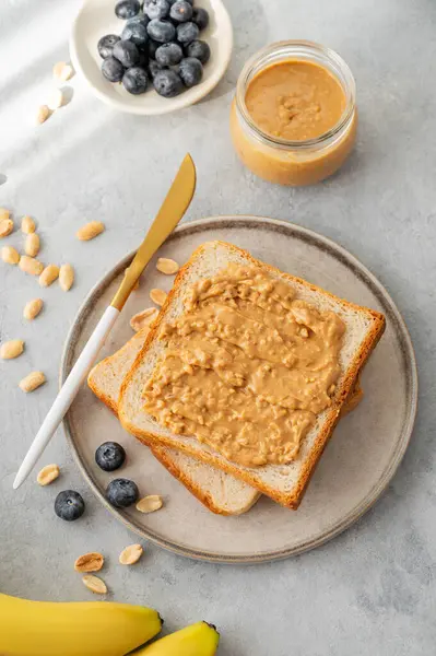 Fıstık ezmeli tost hafif bir arka planda muzlu, yaban mersinli ve sabah gölgeli. Amerikan kahvaltısı için tatlı diyet ve sağlıklı atıştırmalıklar kavramı. Üst görünüm ve kopyalama alanı.