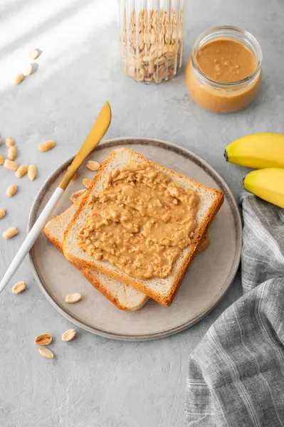 Fıstık ezmeli tost hafif bir arka planda, muz ve sabah gölgesi olan bir tabakta. Amerikan kahvaltısı için tatlı diyet ve sağlıklı atıştırmalıklar kavramı. Üst görünüm ve kopyalama alanı.