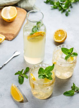 Limonlu, naneli ve buzlu iki bardak taze limonata. Arka planda hafif bir şişe, taze bitki ve meyve var. Yaz modasına uygun mojito mocktail konsepti. Üst görünüm