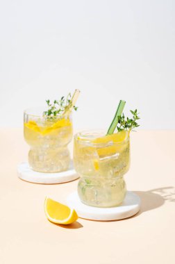 İki bardak limonlu limonata, kekik ve gölgeli açık arkaplanda buz. Yaz modasına uygun mojito mocktail konsepti. Ön görünüm, boşluğu kopyala