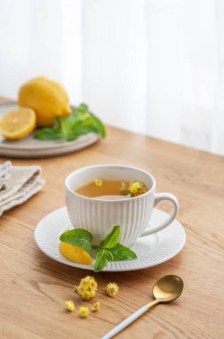 Limonlu, ballı ve naneli bir fincan bitki çayı. Sabah ışıklarıyla pencereye yaslanmış ahşap masa üstü. Kahvaltıda sağlıklı detoks içeceği kavramı. Boşluğu kopyala.