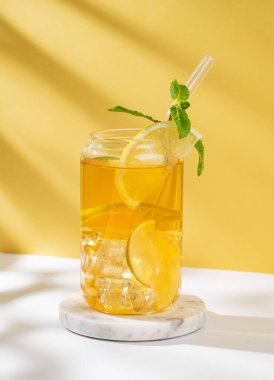 Limonlu buzlu çay ve güneş ışığıyla beyaz sarı arka planda bir bardakta nane şekeri. Yaz günü ferahlatıcı içecek ya da limonata konsepti. Ön görünüm, boşluğu kopyala.