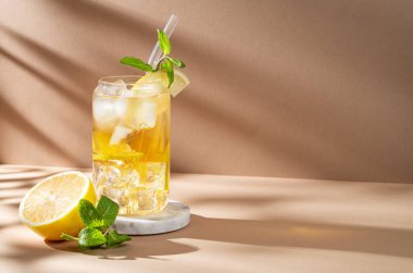 Limonlu buzlu çay ve bej arka planda bir bardakta nane şekeri. Turunçgil meyvesi ve güneş ışığı. Yaz günü ferahlatıcı içecek ya da limonata konsepti. Ön görünüm, boşluğu kopyala.