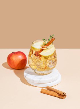 Elma kokteyli ya da elma şarabı buzlu, tarçınlı ve kekikli beyaz bej arka plandaki mermer tezgahta. Reklamcılık ya da bar menüsü afişi için canlandırıcı içecek konsepti. Ön görünüm, boşluğu kopyala