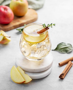Soğuk elma kokteyli ya da buzlu bir bardakta elma şarabı, tarçın ve kekik ile süslenmiş, mermer tezgahta meyvelerle süslenmiş. İçecek konseptini tazelemek. 