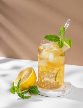 Limonlu buzlu çay ve beyaz bej arka planda bir bardakta nane şekeri. Turunçgil meyvesi ve güneş ışığı. Yaz günü ferahlatıcı içecek ya da limonata konsepti. Ön görünüm, boşluğu kopyala.