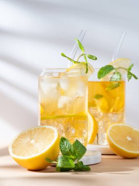 İki bardak limonlu buzlu çay, naneli ve buzlu mermer tezgahta güneş ışığı ve narenciye meyveli. Bir yaz günü kokteyl ya da limonata konsepti. Ön görünüm, boşluğu kopyala.
