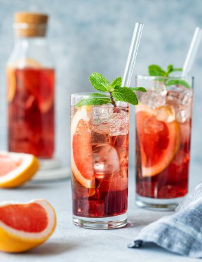 İki bardak limonata greyfurtlu, naneli ve buzlu mavi arka planda doğal ışık, şişe ve narenciye meyveli. Yaz içeceği veya kokteyl konsepti. Ön görünüm ve boşluk kopyala.