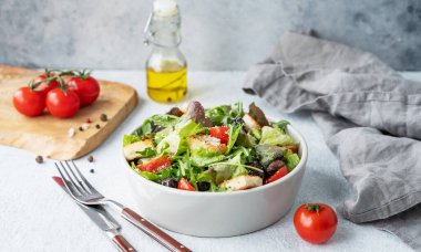 Marul, domates, kızarmış ekmek, zeytin ve parmesan peynirli vejetaryen salatası hafif bir arka planda taze sebze, yağ ve çatal bıçakla birlikte. Sağlıklı beslenme konsepti. 