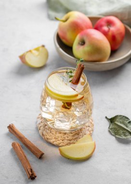 Soğuk elma kokteyli ya da buzlu bir bardakta elma şarabı, tarçın ve kekik ile süslenmiş hafif bir arka planda meyvelerle. İçecek konseptini tazelemek. 
