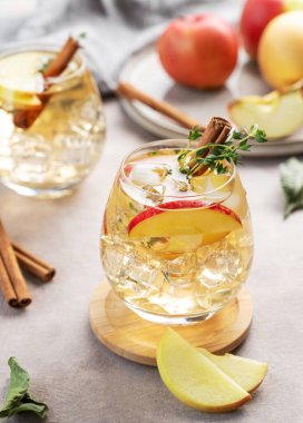 İki bardak soğuk elma kokteyli ya da tarçın ve kekik ile süslenmiş buzlu elma şarabı hafif bir arka planda meyve dilimleriyle. Ferahlatıcı içecek konsepti. Üst görünüm.